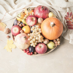 Naklejka na ściany i meble Autumn food concept. Fruits, vegetables and nuts on wooden round tray on light brown background.