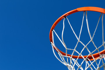 Fototapeta na wymiar Detail of an orange basketball rim (hoop) and white net against blue sky seen from below