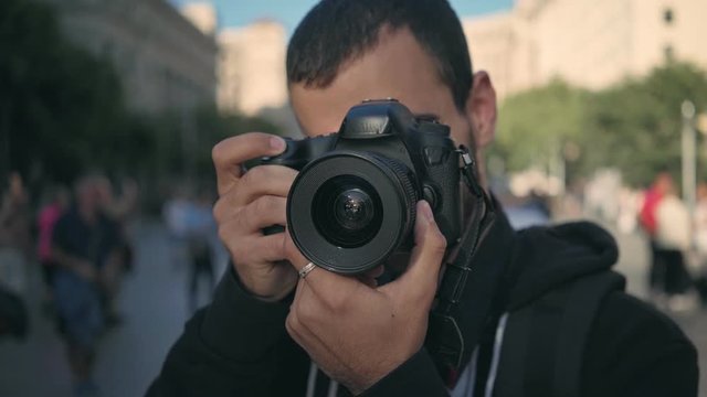 Young man in 20s walks around big city, makes photos of touristic attractions and historical landmarks, clicks and pushes button of shutter release, checks results and smiles, happy memories