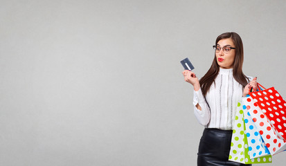 The brunette woman in a shirt and skirt with credit cart  and packeges in hands on a gray background. Place for text.