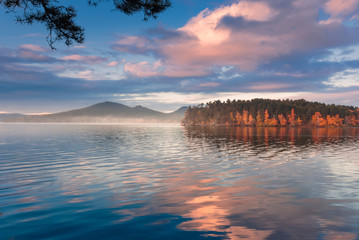 Beautiful foggy autumnal landscape with mountain lake. Pine tree branch on foreground.