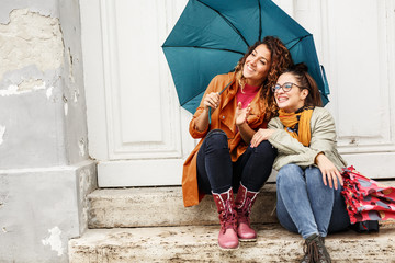 Two female best friends sitting on stairs at the old city downtown.Raining day and autumn concept.