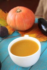 Pumpkin soup in white mug on blue table. Harvest composition.