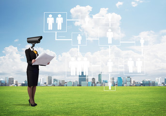 Camera headed woman standing on green grass against modern cityscape