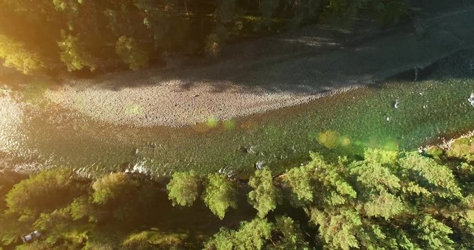 Aerial UHD 4K view. Mid-air flight over fresh and clean mountain river with rock stone bank at sunny summer morning. Green trees and sun rays. Vertical movement