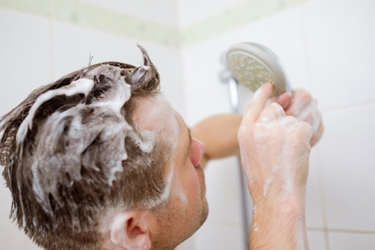 A Young Man With A Soapy Head Is Standing In The Bathroom And Looks At The Shower With Perplexity.