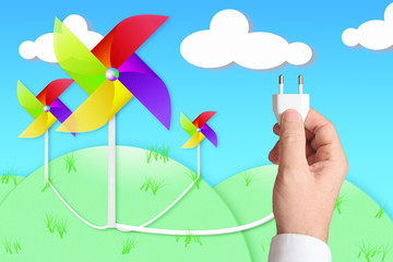 A hand holding a plug connected to some windmill. Renewable energy concept.