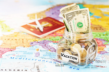 Vacation money savings in a glass jar with passport and aircraft toy on world map, selective focus
