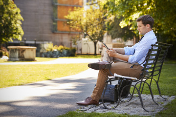 Fototapeta premium Businessman Outdoors Using Digital Tablet On Lunch Break In Park