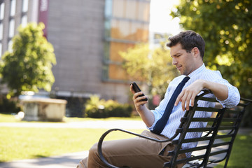 Fototapeta premium Businessman Outdoors Using Mobile Phone On Lunch Break In Park