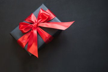 Gift box in black paper with red ribbon on black surface. Top view.