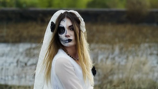 The portrait of young woman with spooky make-up for Halloween in a white bride dress. 4K