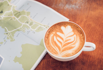 White coffee cup with latte art with travel map on brown wood table,Leisure activity