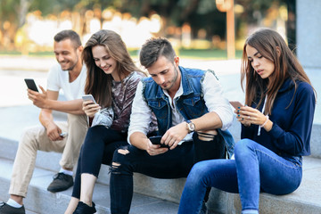 Two young men and women use telephone sitting on stairs