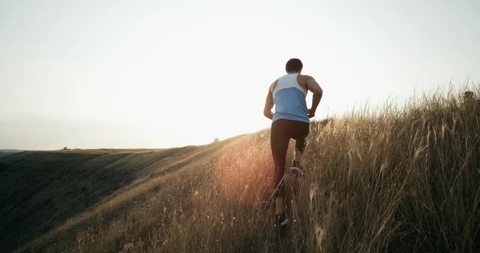 Running runner man jogging at sunset. Male jogger training for marathon run running up hill in silhouette against colorful yellow sky. Fit fitness model living healthy active outdoor lifestyle. 4k