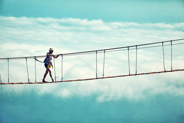 Woman is walking along a suspension bridge over an abyss.