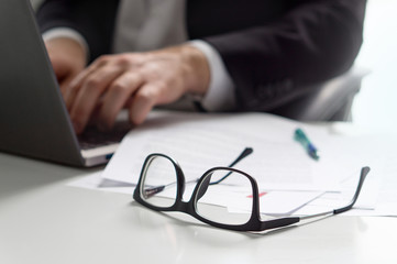Business man writing with laptop in office with glasses on table.