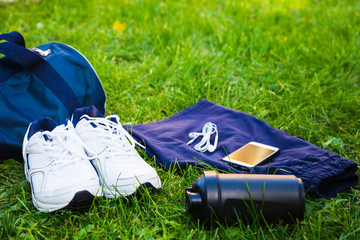 Fototapeta na wymiar A sports bag with sneakers, shaker, shorts, phone and headphones for running on the grass