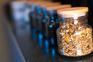 Different types of tea in glass jars on a blurred background.