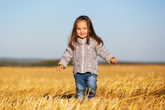 Happy 2 year old girl walking in a summer harvested field