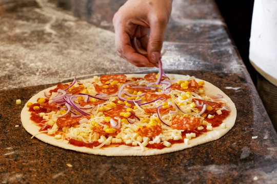 Cook's hands putting red onion on tomato base pizza.