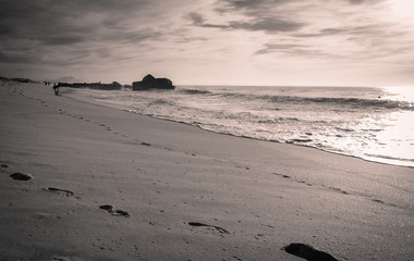 silhouette of people enjoying on sandy beach with waves hot sunny day in october on atlantic coast in black and white with red filter, capbreton, france