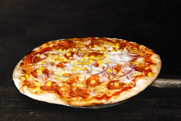 Baked salami pizza on metal paddle isolated on dark grey background.