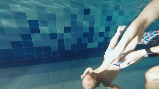 The family is swimming in the pool. The father is teaching his son. The little son successfully copes with the attempt to lift the object from the bottom of the pool.