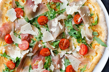 Detail of prosciutto pizza with cherry tomatoes and rucola from above.