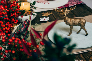 toy golden reindeer, on the plate at the Christmas table, surrounded by nandinas