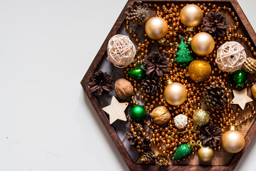 Beads, gold and green balls. New Year composition in wooden plate.pine cones and Christmas tree decorations on wooden, white background. Copy space. Selective focus.Top view