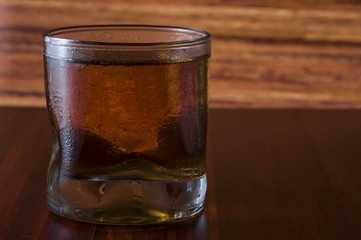 Glass of wiskey and ice on wooden background