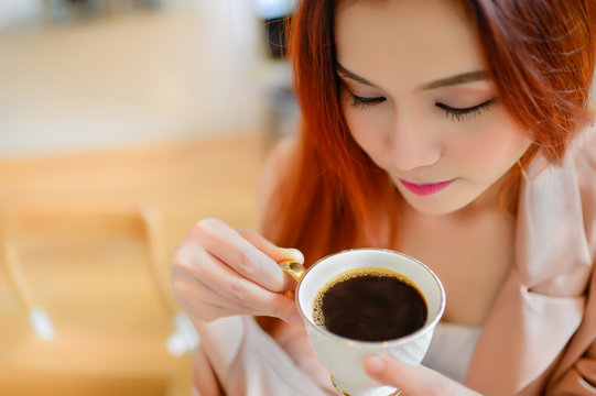 Portrait of beautiful face woman and holding a cup of coffee in her hand in blur background coffee shop, she drink coffee in the morning