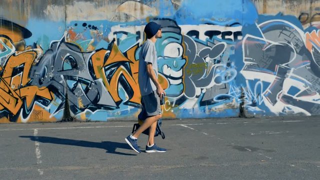 A male graffiti artist walks along a painted wall. 
