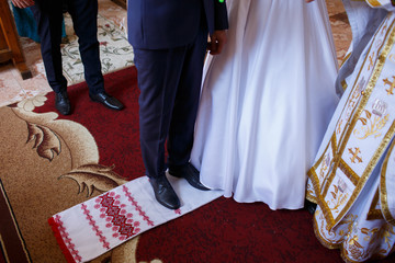 Wedding couple standing on the embroidered towel in the church during the wedding ceremony