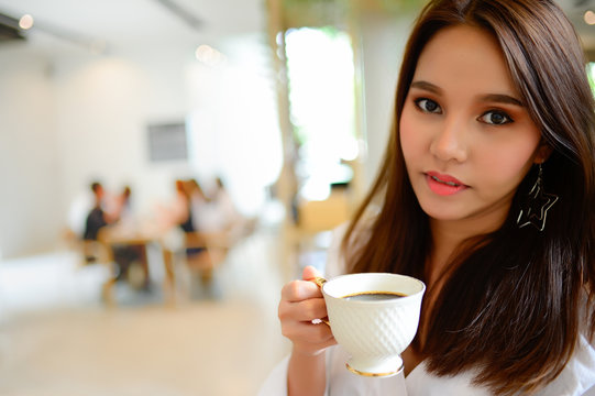 Portrait of beautiful woman holding a cup of coffee in her hand in blur background coffee shop, she drink coffee in the morning