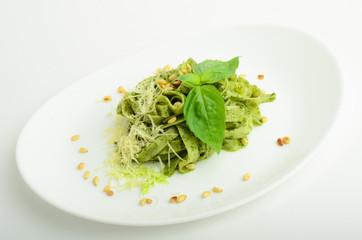 Pesto pasta with cheese and pine nuts decorated basil on a plate isolated on white background