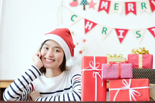 Young cute asian woman wearing santa hat and smiling beside Christmas gift boxes, Christmas people celebration concept