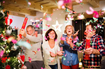 Senior friends with confetti poppers next to Christmas tree.