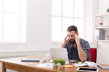 Young stressed businessman with laptop in modern white office