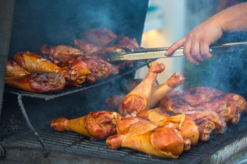 Barbecue from chicken legs, on a metal brazier and grate, with smoke, tongs in hand. BBQ in the open air.