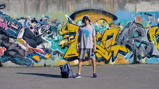 A graffiti artist stands still near his work.   