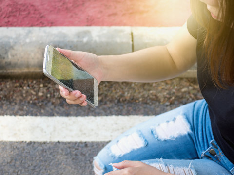 Woman picking up and holding cracked screen smart phone from the ground