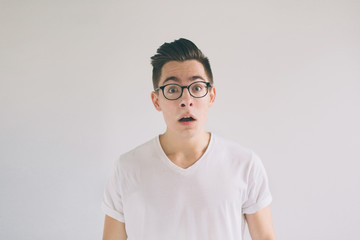 Omg! No way! Very shocked young man with glasses is looking at the camera. Student nerd is wearing in a white t-shirt, standing isolated on a white background