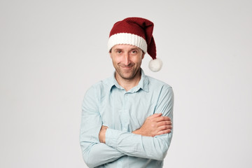 Relaxed mature man wearing santa claus hat standing with hands crossed on white background.