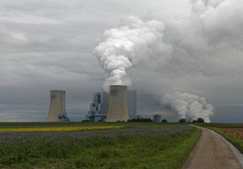 Elektrizitätswerk mit Emissionen, düsteren Wolken und Feldern
