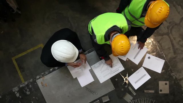 Workers and manager in safety helmets working with documents at factory