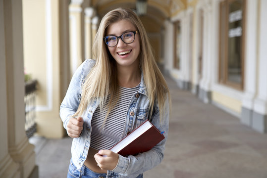 young woman student with long hair and glasses happily dancing emotionally with the book in his hands. Portrait with natually light