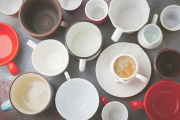 Empty colorful cups and one cup of coffee.Various dishware on a background of gray concrete or stone background. Selective focus.Top view. Copy space.