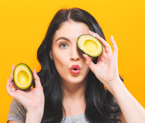 Happy young woman holding avocado halves on a solid background
